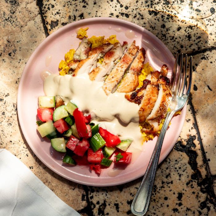 Sliced chicken over saffron rice with cucumber tomato salad and tahini sauce